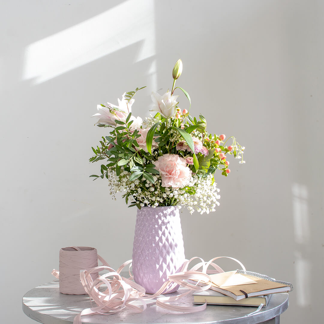 Ramo de flores en tonos rosas decorando una mesa.